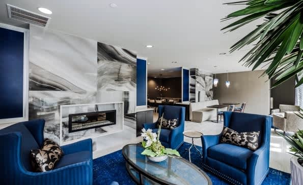 Contemporary living room with blue armchairs, linear fireplace, marble accent wall, and potted plant.