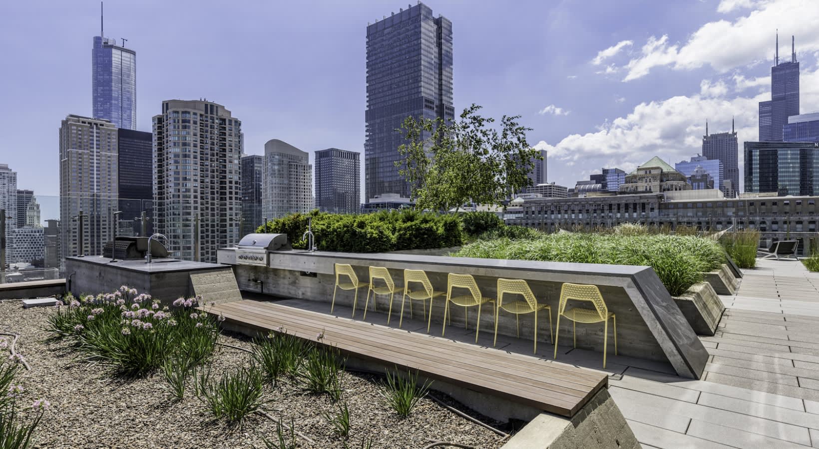 Rooftop terrace with yellow chairs, wooden bench, gravel planting beds, and Chicago skyline backdrop.