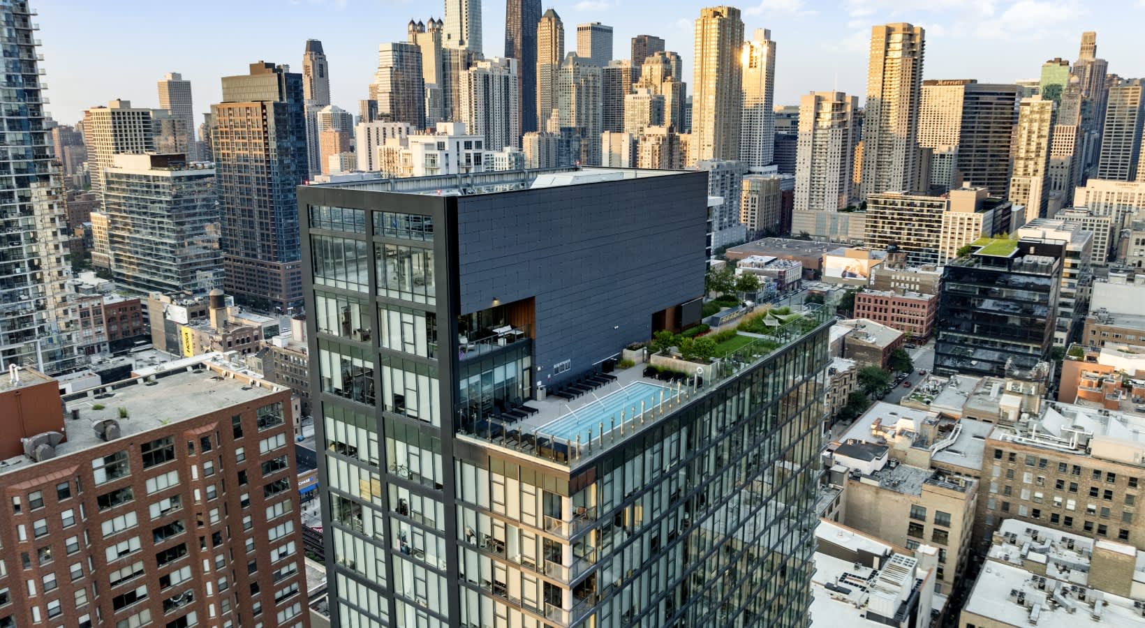 Modern high-rise building with rooftop pool and green space overlooking Chicago's downtown skyline.