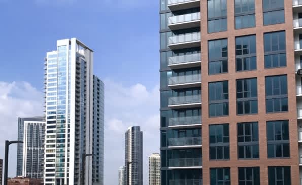 View of multiple high-rise residential buildings in Chicago, including a brick and glass tower with balconies against a blue sky.