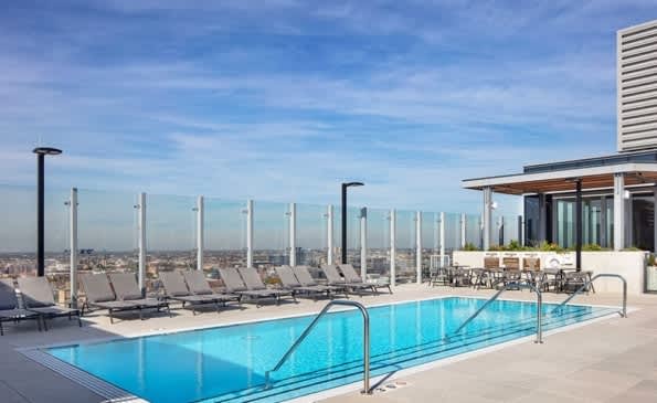 Rooftop pool with blue water, lounge chairs, glass wind barriers, and Chicago cityscape view under clear sky.