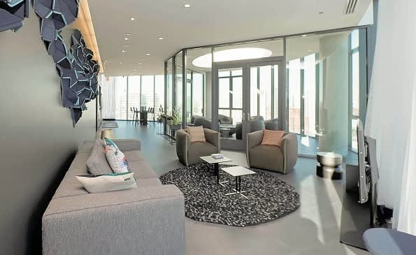 Open-concept living room with gray sofa, armchairs, round black rug, and glass partition walls overlooking additional seating areas.