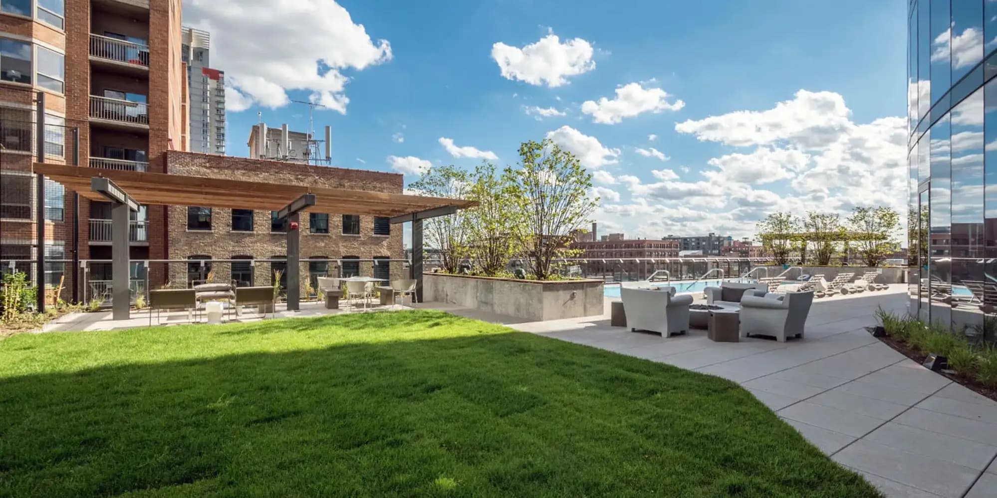 Rooftop terrace with green lawn, wooden pergola, lounge seating, and Chicago skyline views under blue sky.