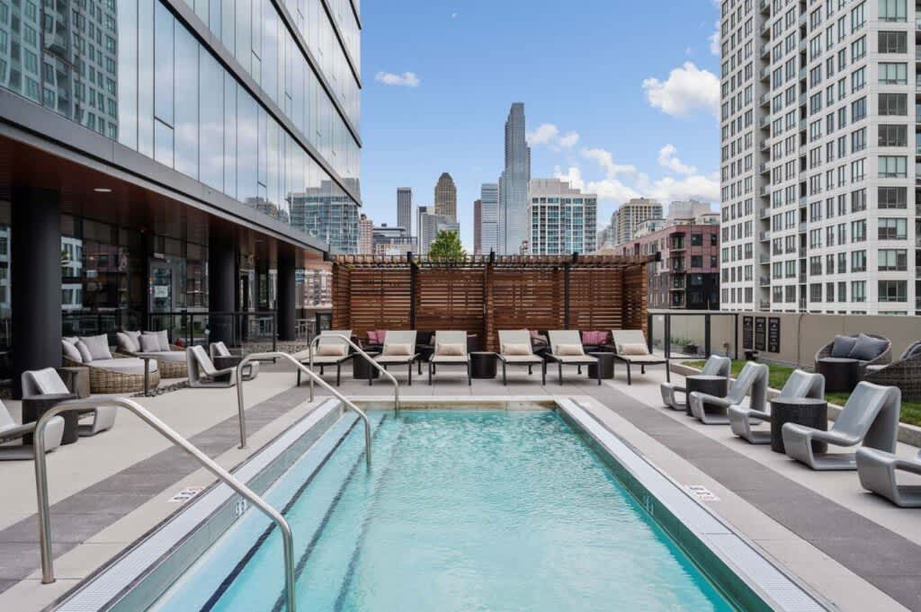 Rooftop pool with clear turquoise water, lounge chairs, wooden privacy screen, and downtown Chicago skyline in background.