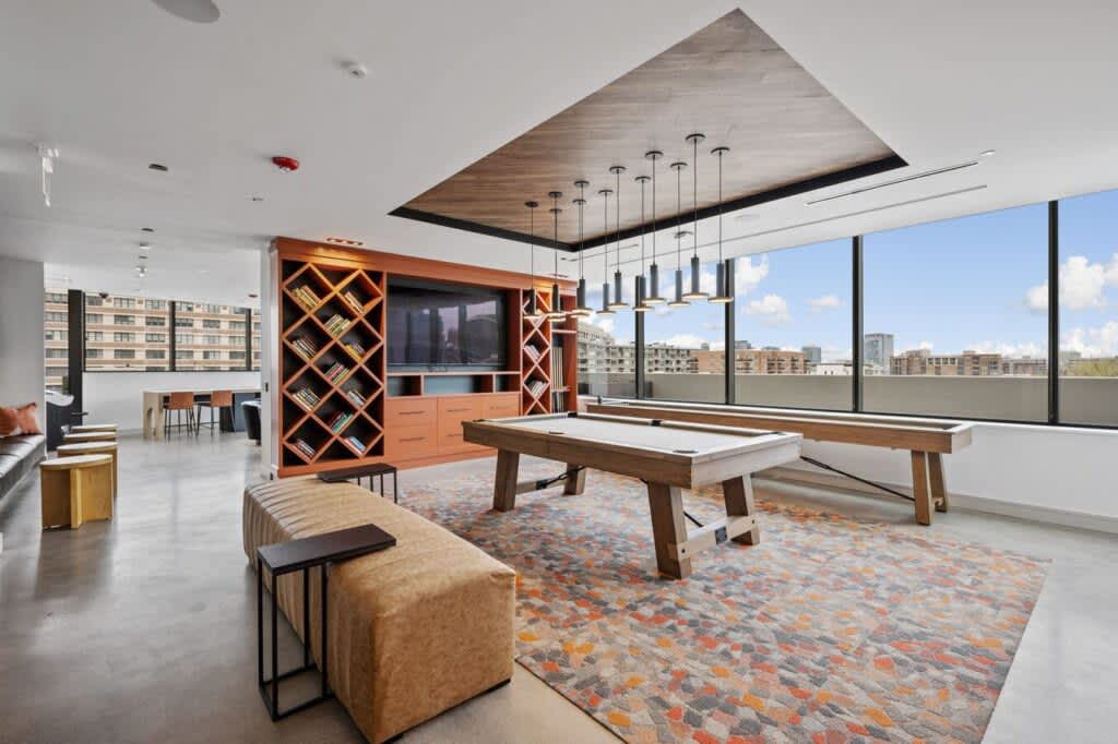 Recreation room with pool table, geometric wood shelving, pendant lights, and panoramic city views from floor-to-ceiling windows.