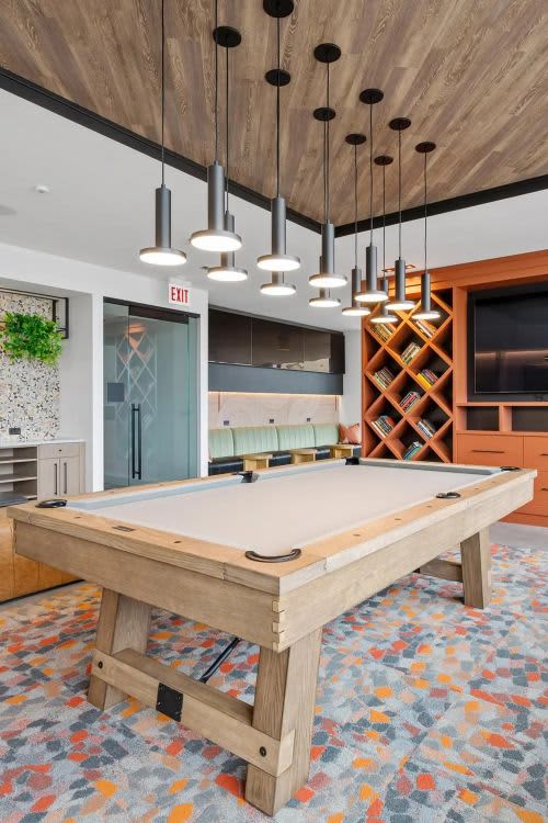 Game room with light wood pool table, hanging pendant lights, orange geometric shelving, and patterned area rug.