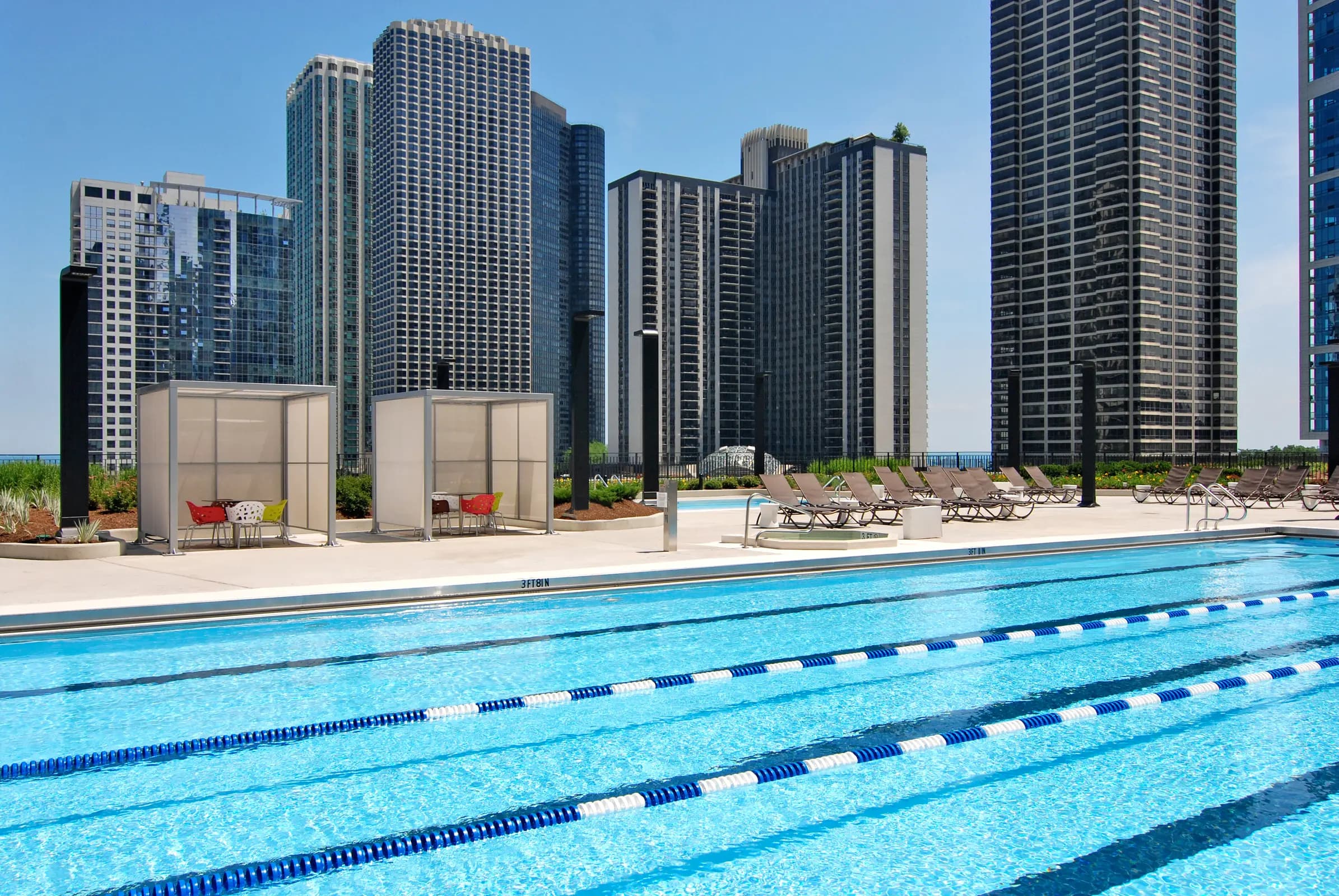 Outdoor lap pool with lane dividers, lounge chairs, cabanas, and downtown Chicago high-rise buildings in background.