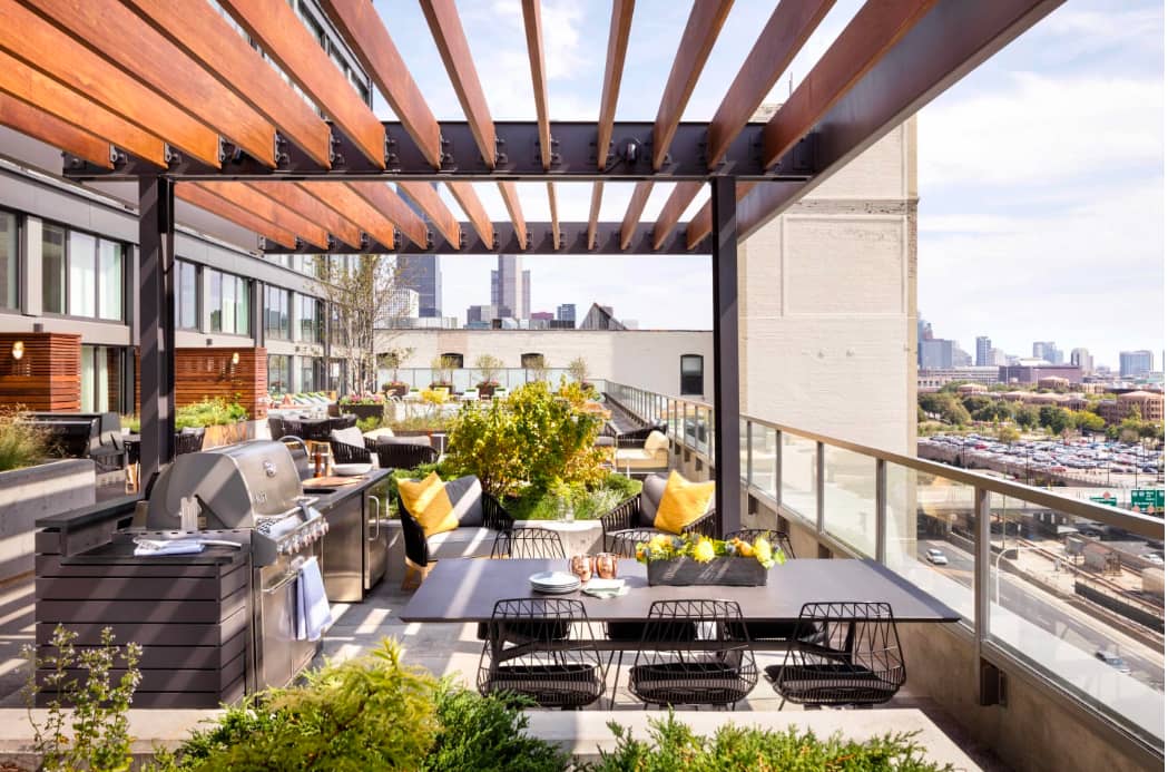 Rooftop terrace with wooden pergola, dining table, lounge seating, planters, and Chicago skyline view.