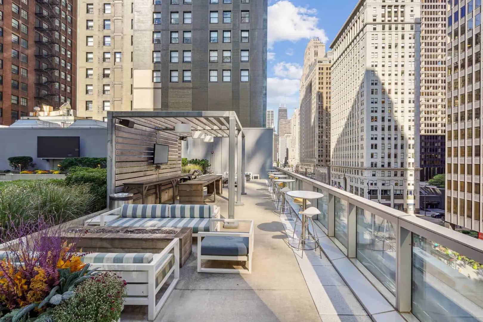 High-rise rooftop terrace with built-in seating, striped cushions, flowering plants, pergola, and downtown Chicago skyline views.