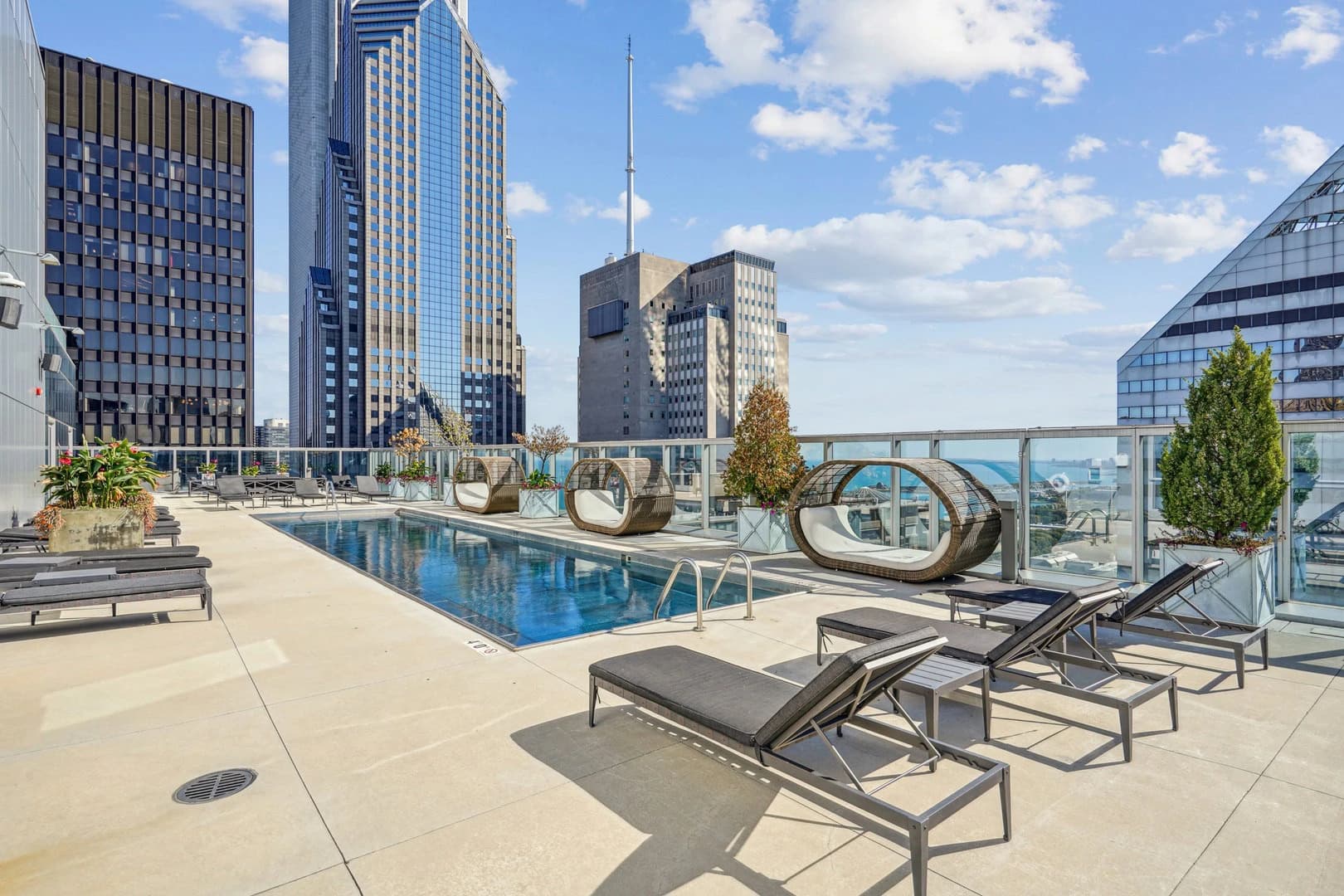 Rooftop pool deck with lounge chairs, rectangular pool, glass railings, and downtown Chicago skyline backdrop.