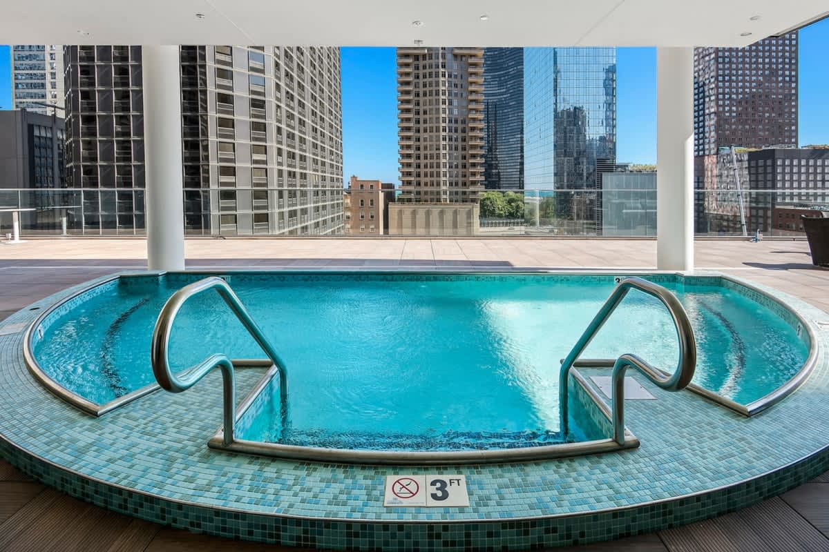 Curved indoor rooftop pool with turquoise water, metal handrails, and floor-to-ceiling windows framing Chicago's downtown skyline and high-rise buildings.