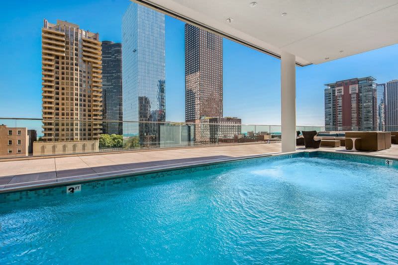 Indoor swimming pool with turquoise water, floor-to-ceiling windows, and Chicago skyline views of tall buildings and clear sky.