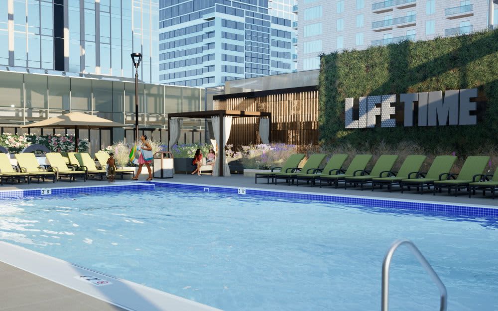 Outdoor swimming pool with blue water, lounge chairs, and high-rise buildings surrounding a modern urban courtyard.