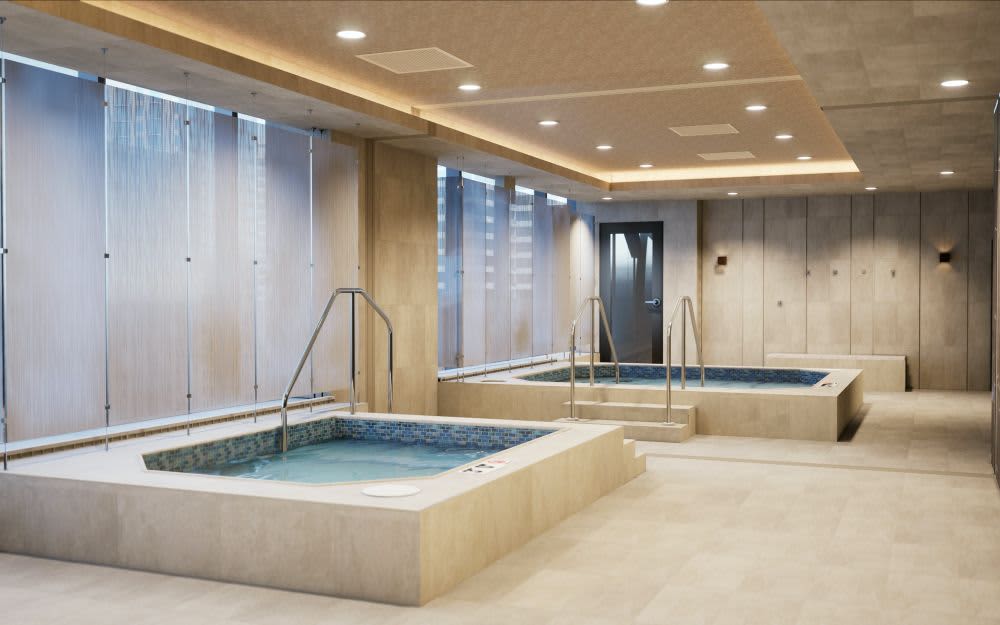 Indoor spa area with two sunken pools with blue tile accents, metal railings, beige stone walls, recessed ceiling lights, and floor-to-ceiling windows.