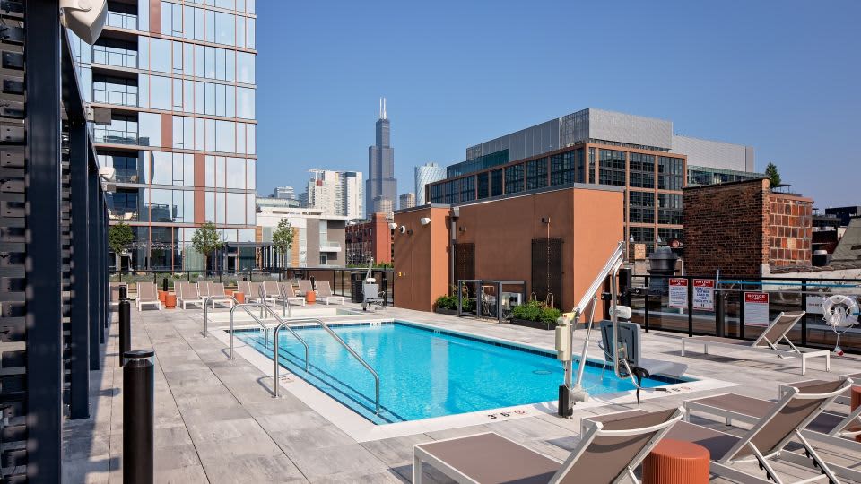Rooftop pool with lounge chairs, glass railings, and Chicago skyline including Willis Tower in background.