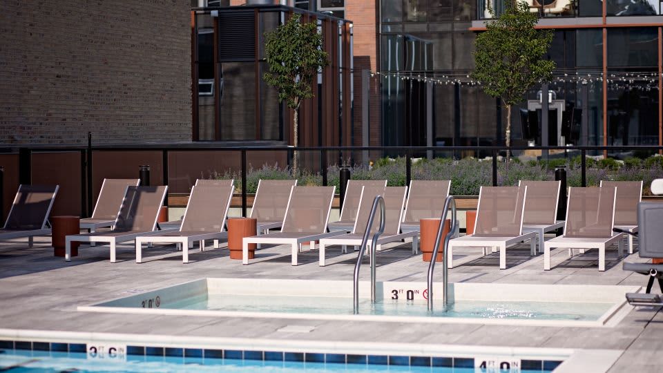 Rooftop pool deck with lounge chairs, hot tub, and brick building backdrop in Chicago.