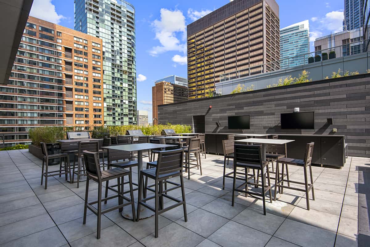 Rooftop terrace with high-top tables, bar seating, and downtown Chicago skyline with residential towers in background.