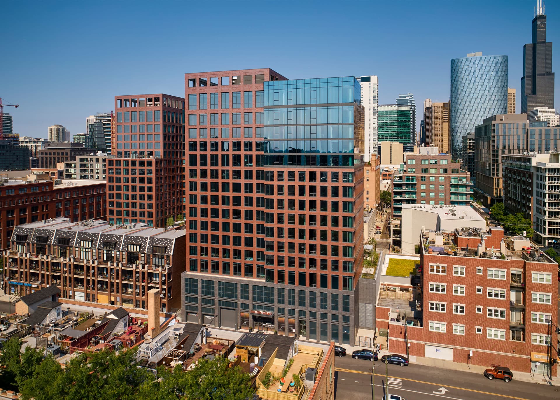 Elevated view of a modern orange and glass high-rise building surrounded by Chicago's downtown skyline on a clear day.
