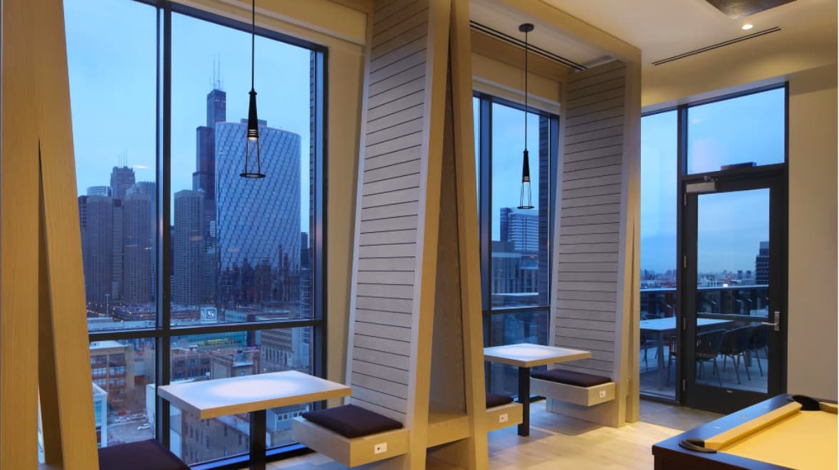 High-rise apartment with floor-to-ceiling windows overlooking Chicago skyline, yellow accent walls, wooden dining tables, and pendant lighting.