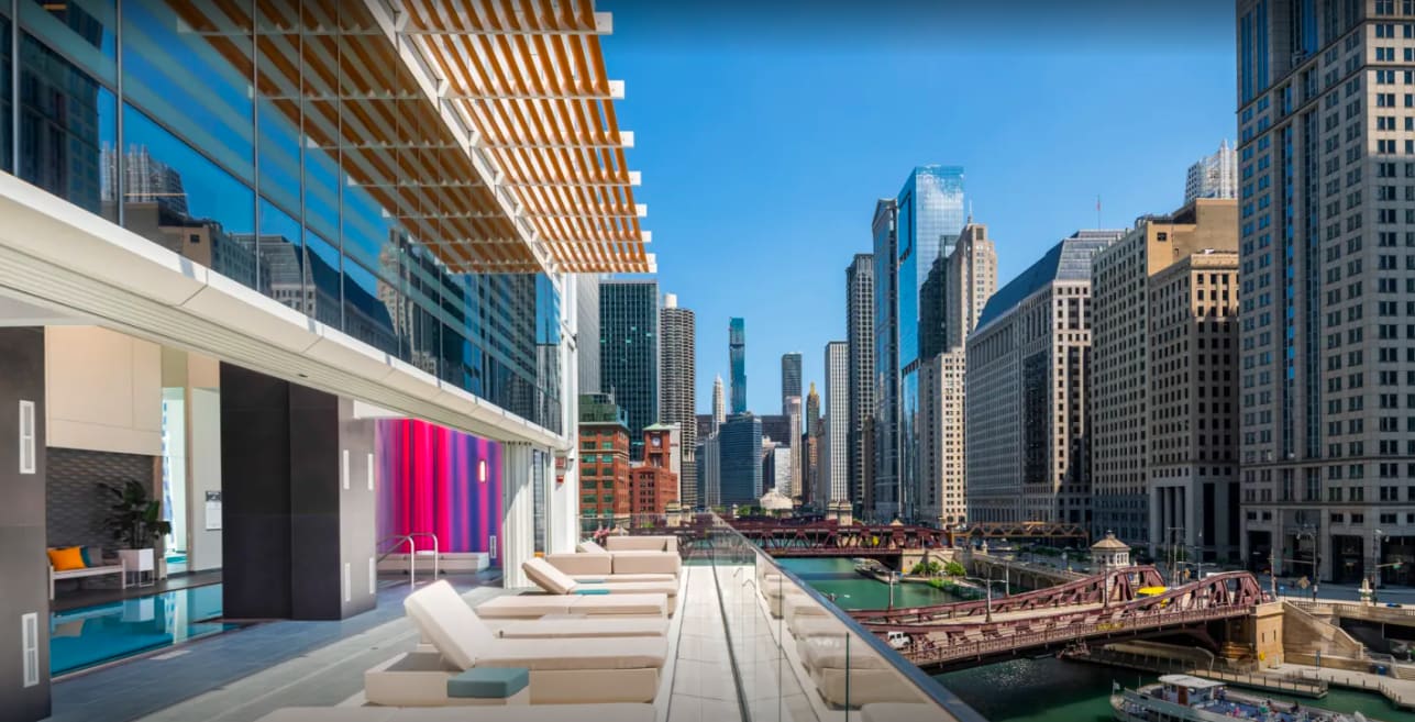 Rooftop terrace with lounge chairs, wooden pergola, and panoramic views of Chicago's downtown skyline and river.