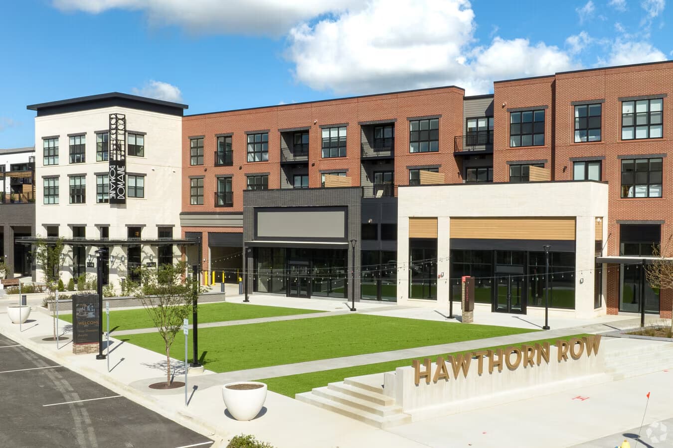 Courtyard with manicured lawn, modern white and black storefronts, red brick residential buildings, and Hawthorn Row signage under blue sky.