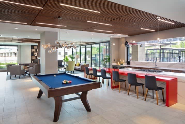 Clubroom with blue pool table, red bar counter with black chairs, lounge seating, and glass doors opening to outdoor space.