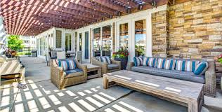 Covered patio with striped awning, wicker seating with blue cushions, brick exterior, and geometric floor pattern.