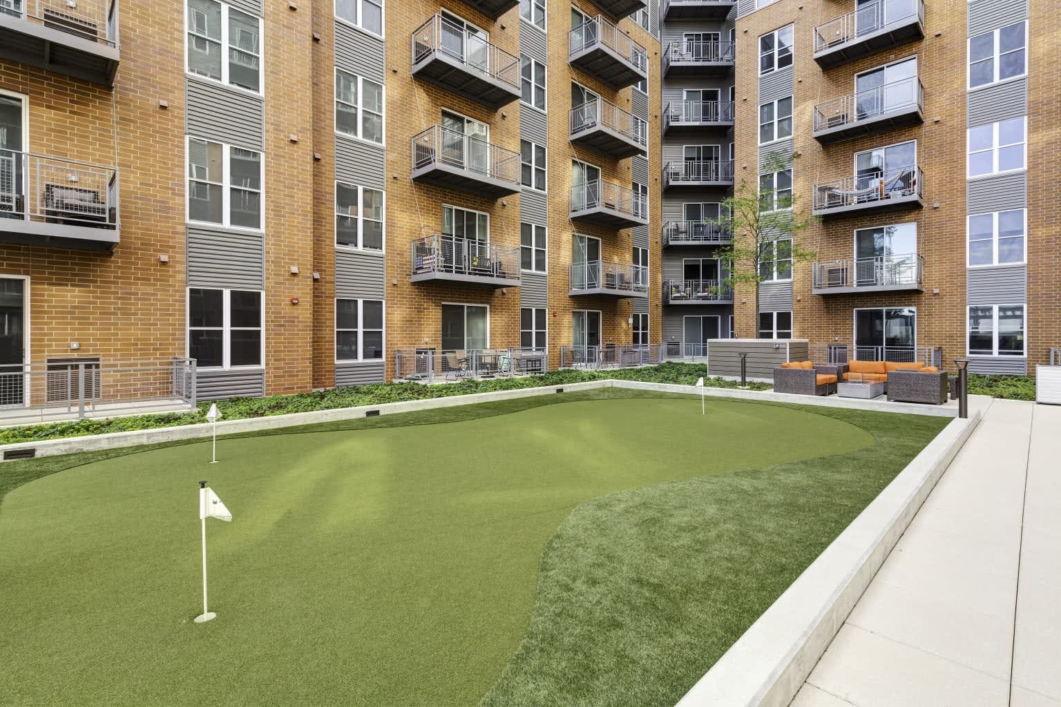 Courtyard with putting green and white flag, surrounded by multi-story brick apartment buildings with balconies and seating areas.