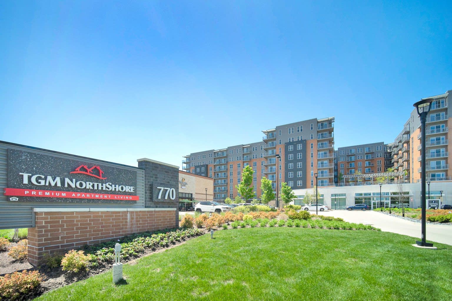 TGM Northshore apartment complex exterior with brick signage, manicured lawn, landscaping, and multi-story residential buildings under clear sky.