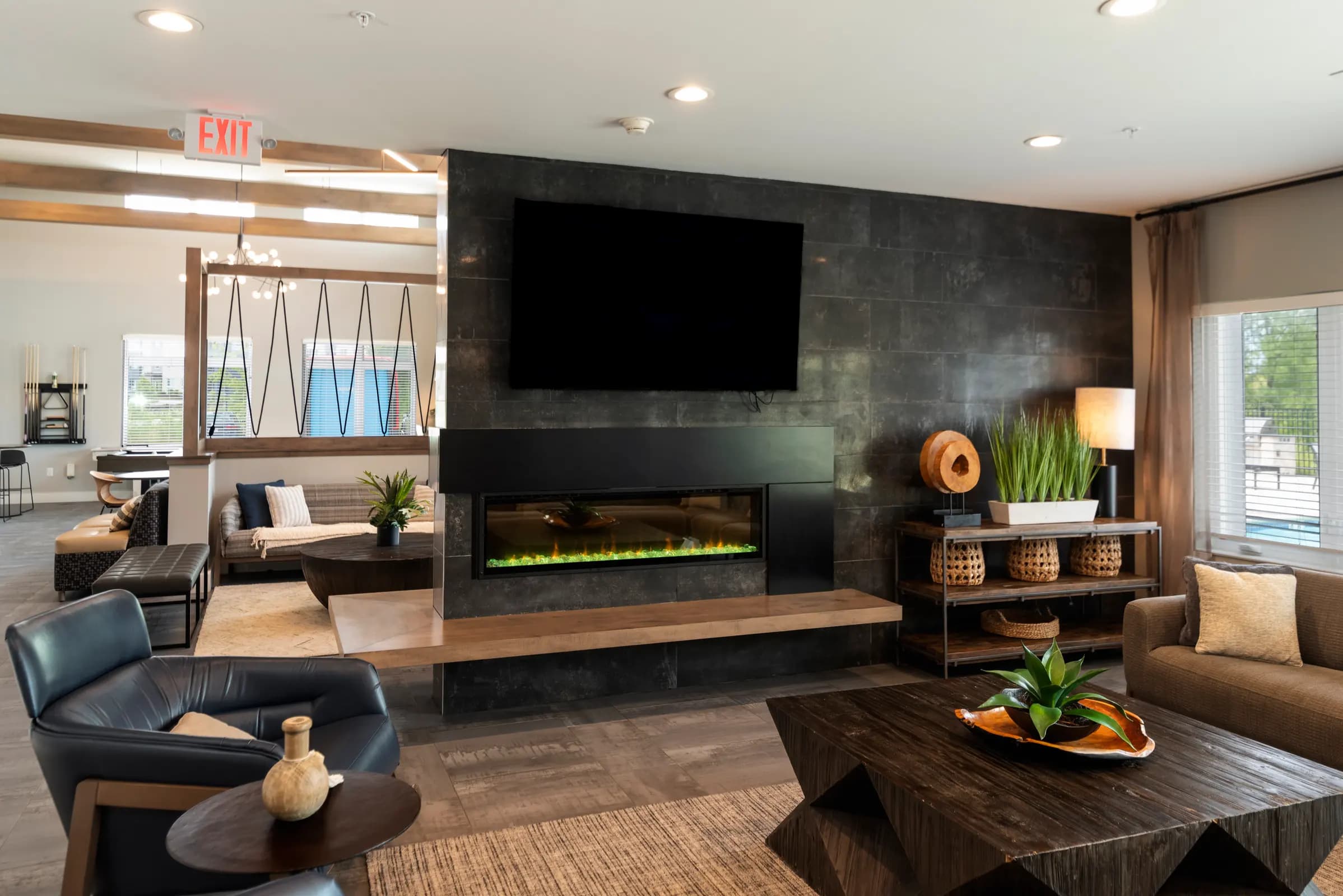 Modern lounge with black accent wall, built-in electric fireplace with green flame effect, wall-mounted TV, and dark leather seating.