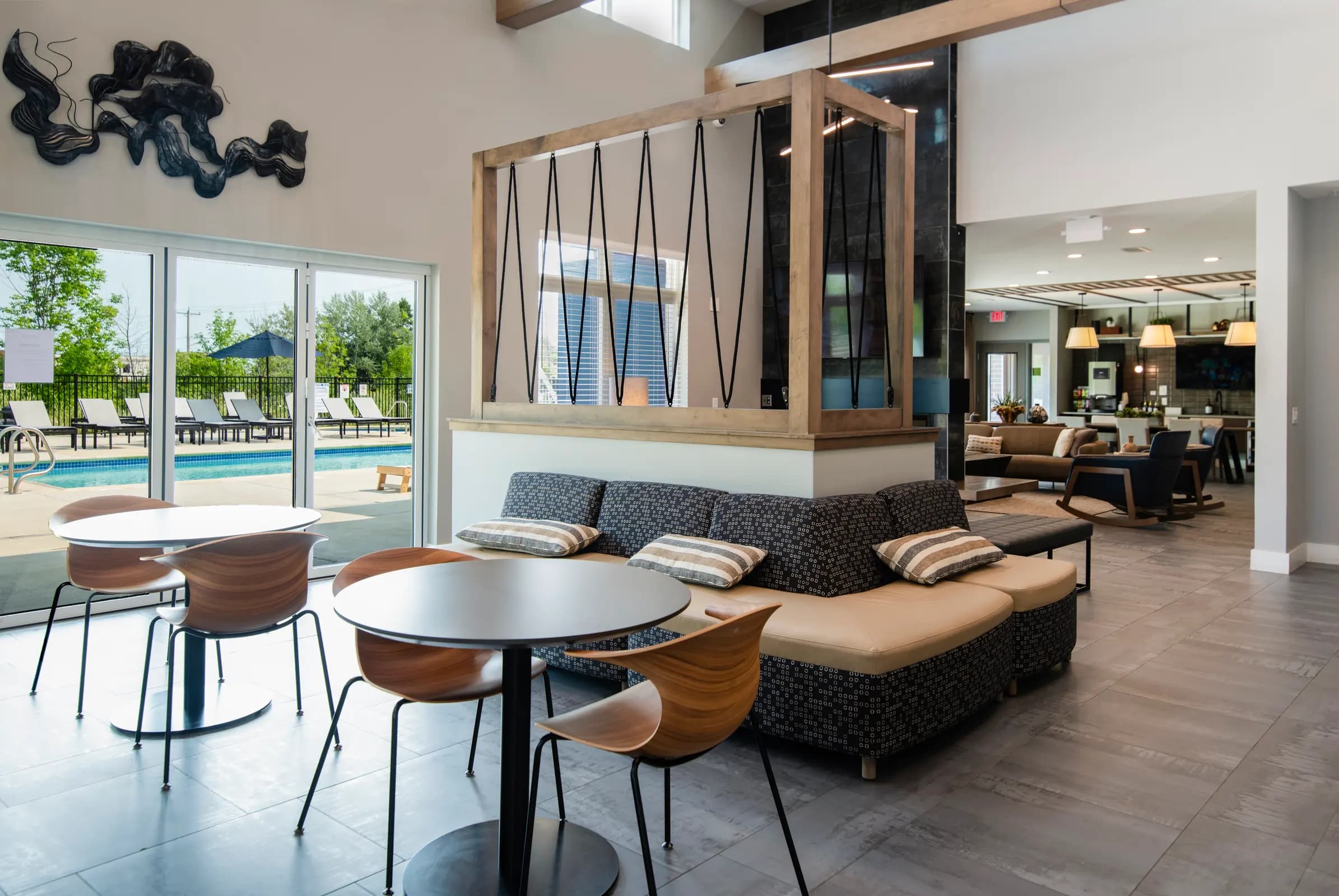 Community lounge with dining table, mid-century chairs, dark upholstered seating, wooden room divider, and view of outdoor pool area.