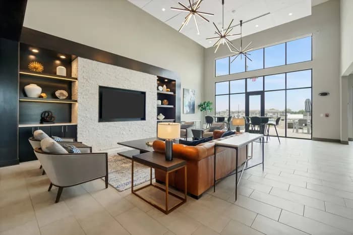 Modern living room with white stone accent wall, wall-mounted TV, orange leather sofa, gray armchair, and expansive windows overlooking the city skyline.