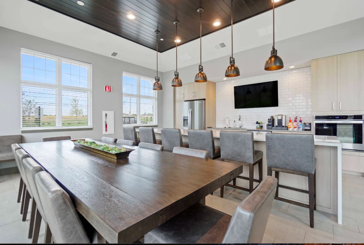 Dining room with dark wood table, gray upholstered chairs, copper pendant lights, and open kitchen with white cabinetry and stainless steel appliances.