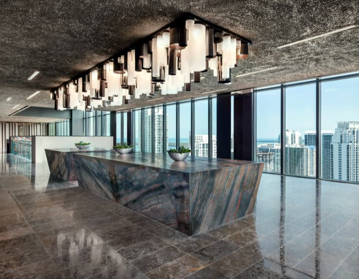 Modern kitchen with sculptural marble island, geometric pendant lighting, and panoramic windows with Miami skyline views.