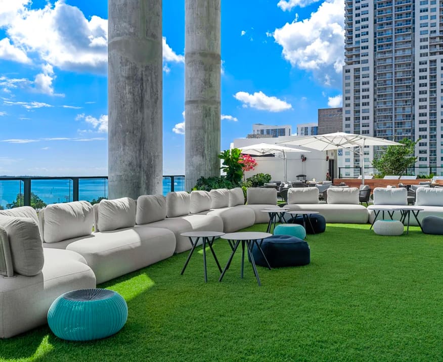 Rooftop terrace with white modular seating, artificial turf, ocean view, and downtown Miami skyline.