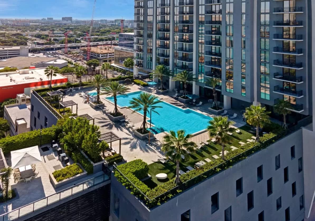 Aerial view of resort pool with palm trees, lounge seating, and modern residential towers in Miami.