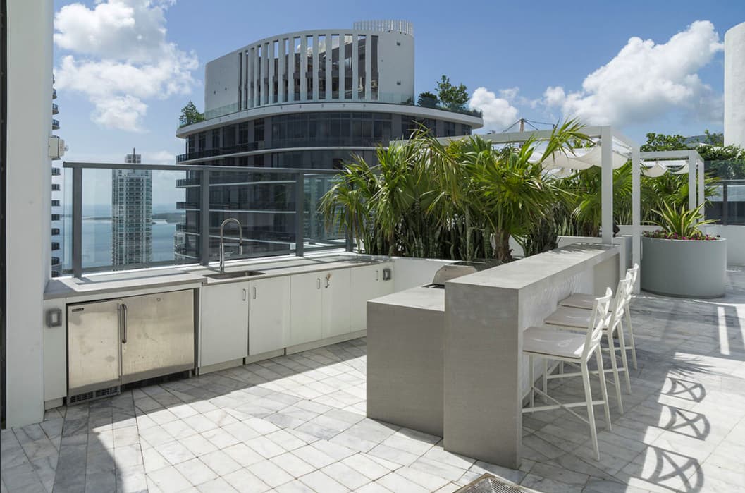 Rooftop terrace with outdoor kitchen, bar seating, potted palms, and waterfront views of Biscayne Bay.