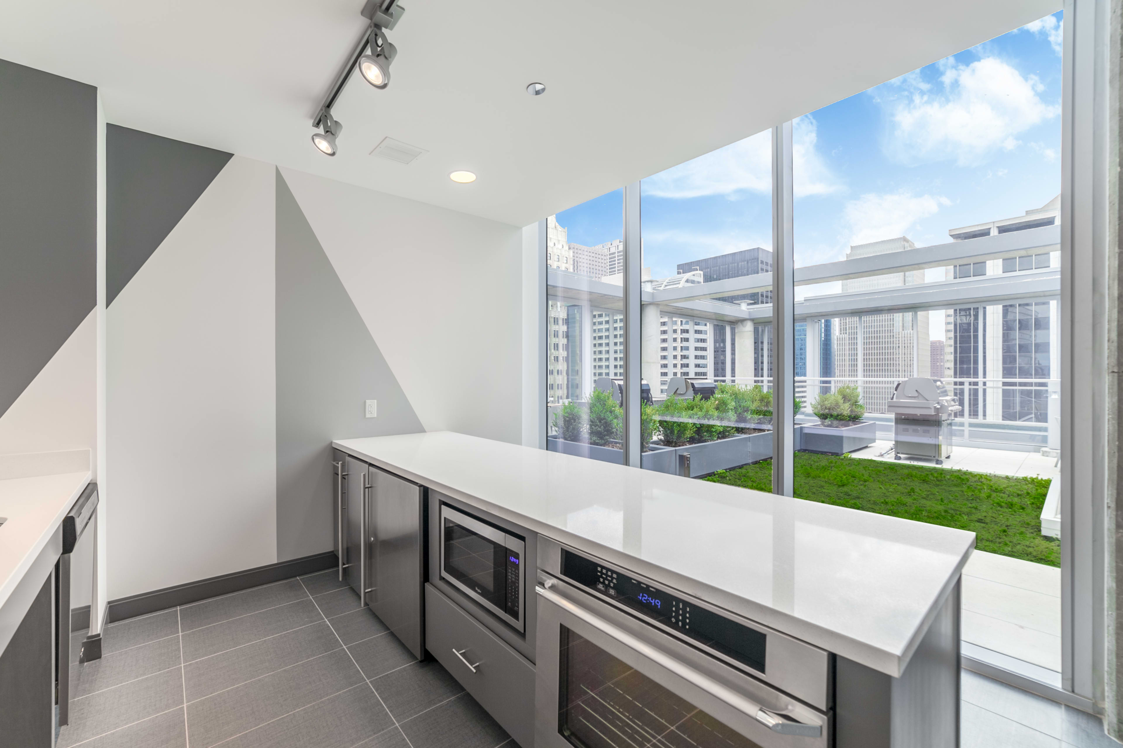 Modern kitchen with white quartz island, stainless steel appliances, and expansive windows opening to a rooftop garden with downtown Chicago skyline views.