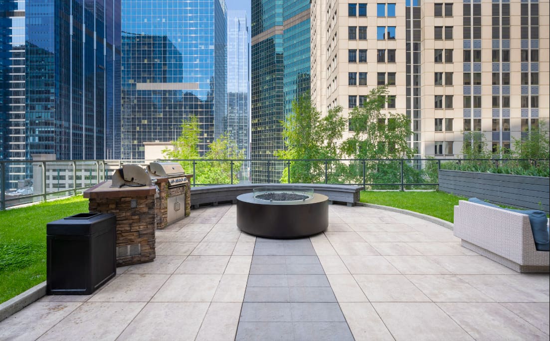 Rooftop terrace with fire pit, built-in grill, seating area, and downtown Chicago skyline views surrounded by tall buildings.