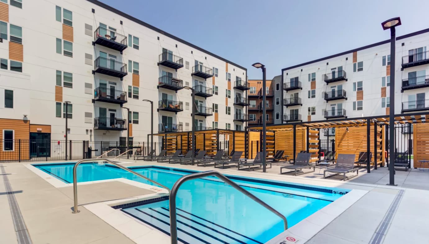 Two bright blue pools with metal railings in a concrete courtyard, surrounded by multi-story apartment buildings with balconies and yellow wooden shade structures.