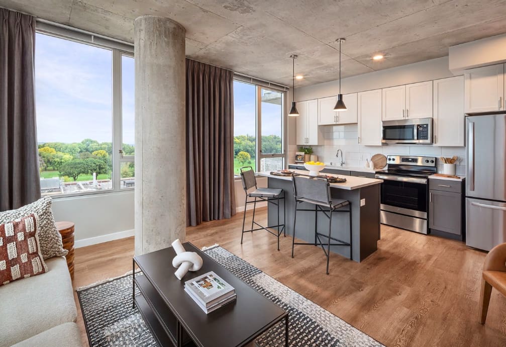 Open-concept apartment with kitchen island, stainless steel appliances, concrete column, hardwood floors, and expansive windows with park views.