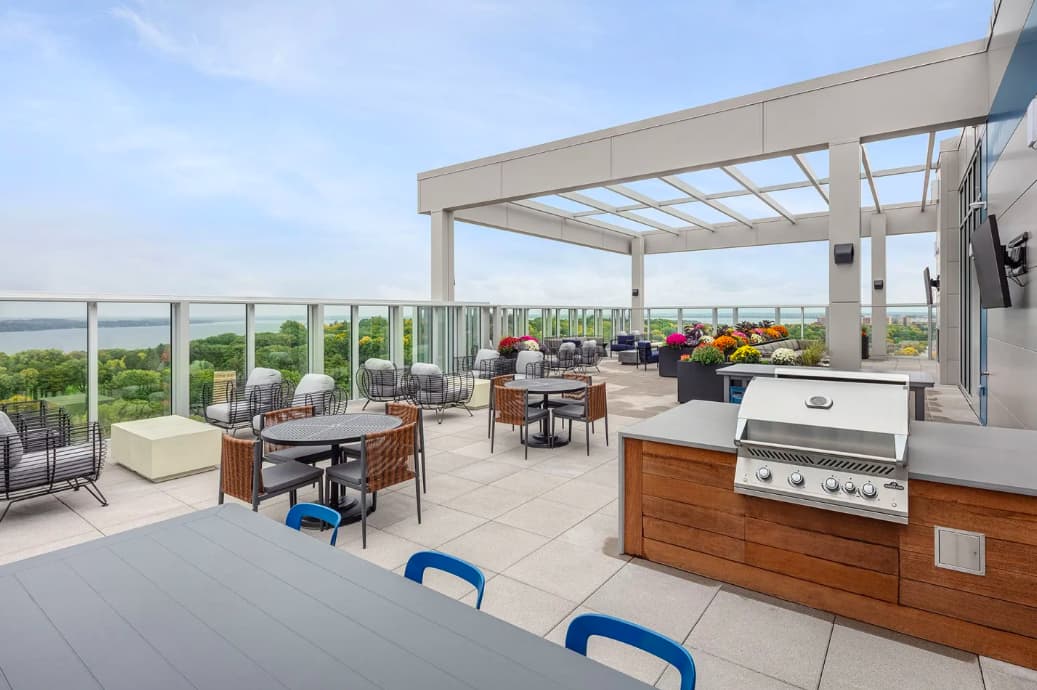 Rooftop terrace with pergola, outdoor kitchen with stainless steel grill, dining tables, lounge seating, and panoramic views of water and green landscape.