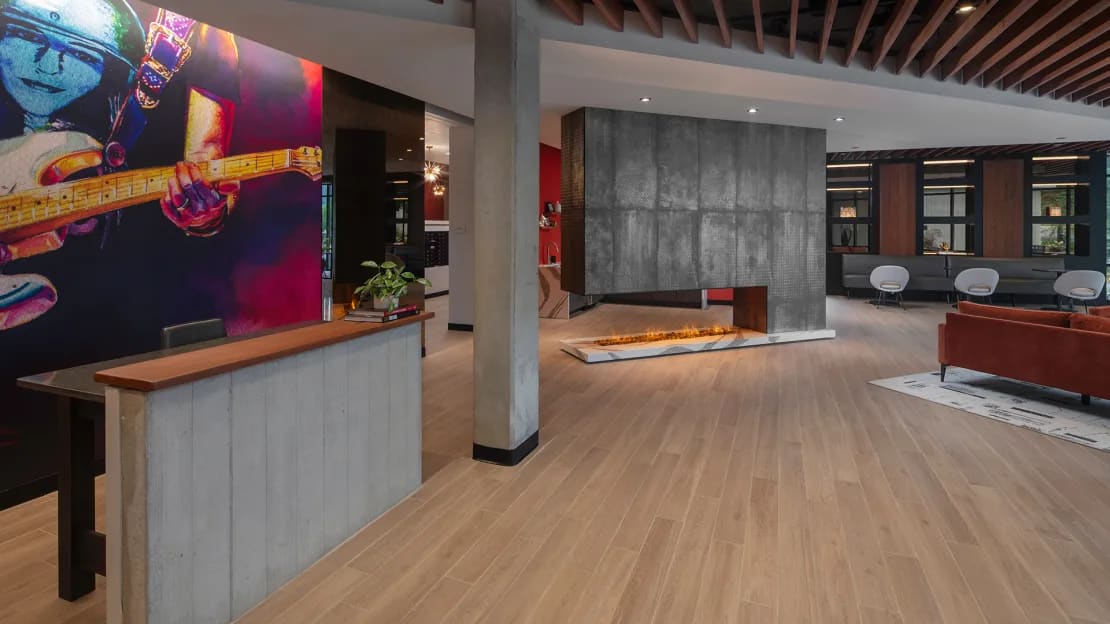 Modern lobby with wood flooring, reception desk, colorful guitar artwork, concrete columns, and seating areas.