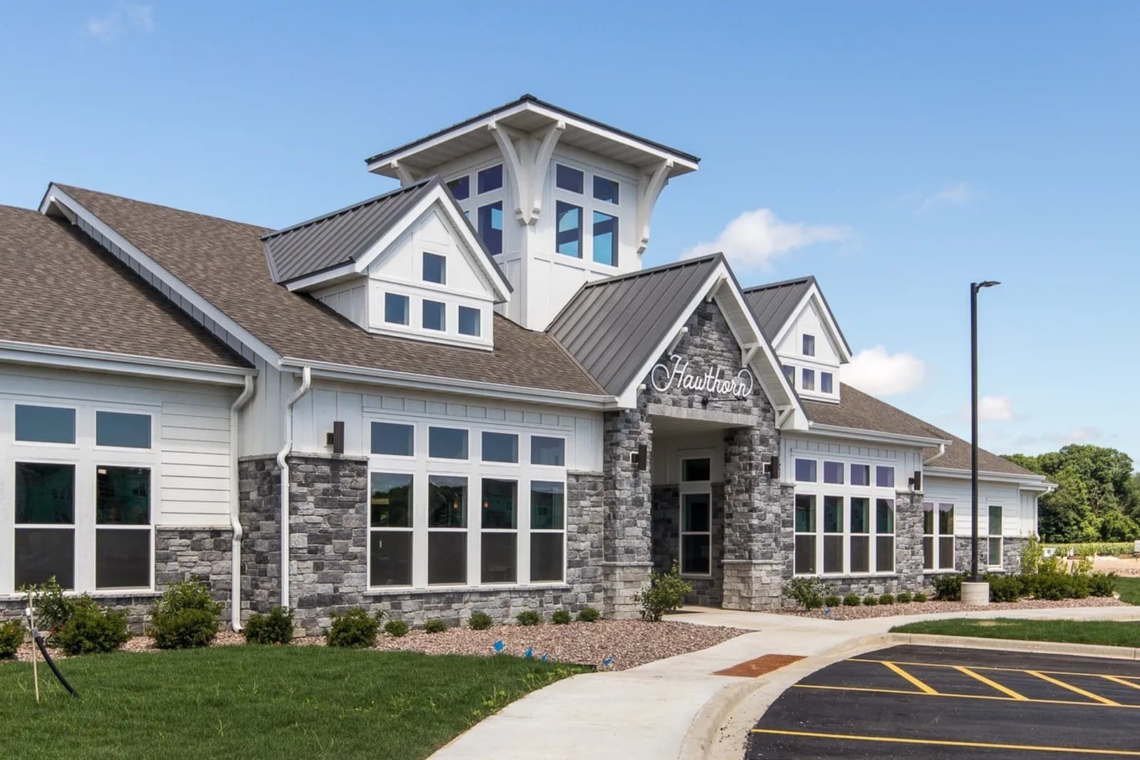 Modern apartment building exterior with stone and white siding, multiple large windows, cupola tower, and manicured landscaping.