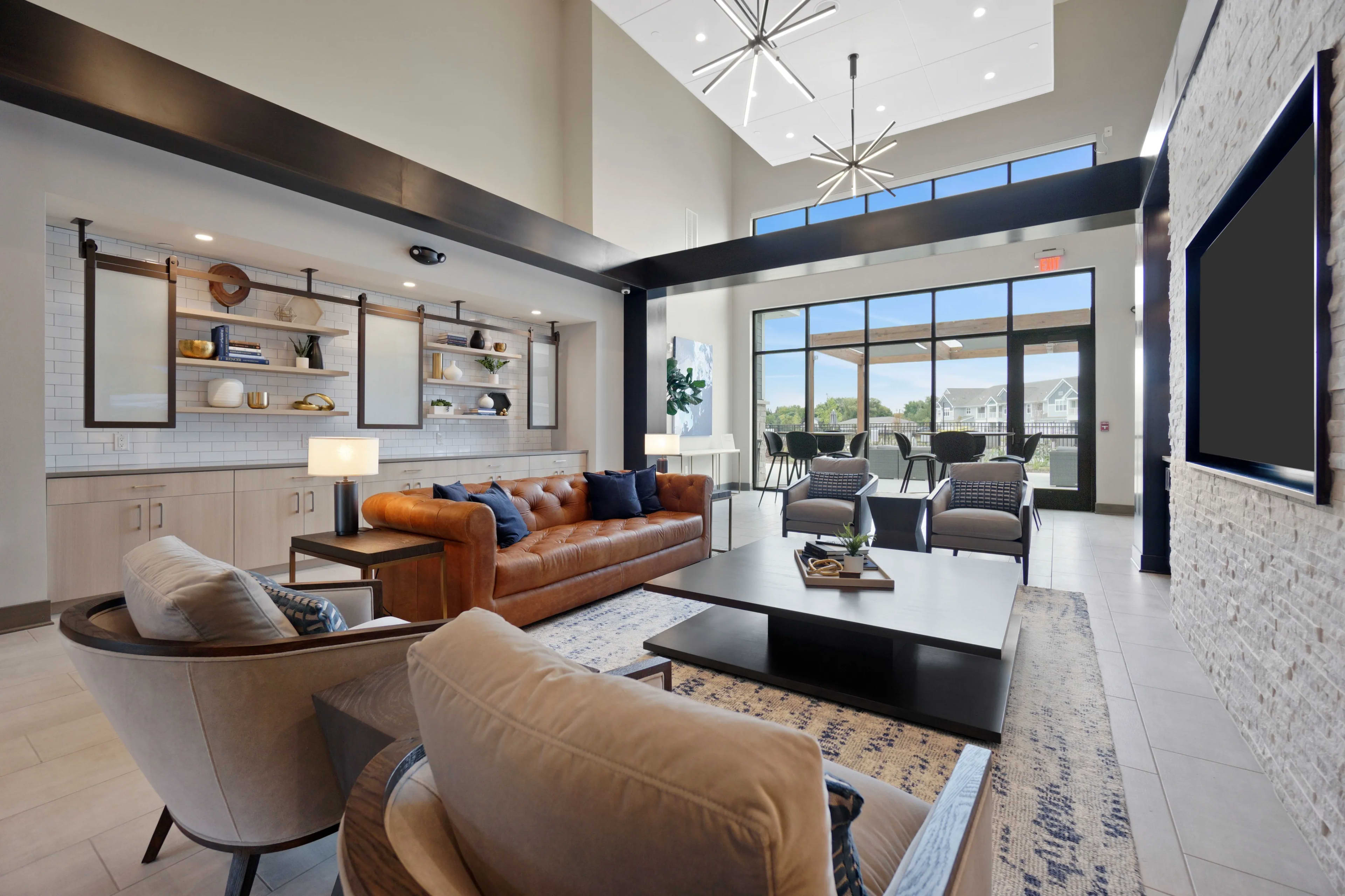 Modern lounge with cognac leather sofa, cream armchairs, black coffee table, skylight, and floor-to-ceiling windows overlooking mountains.