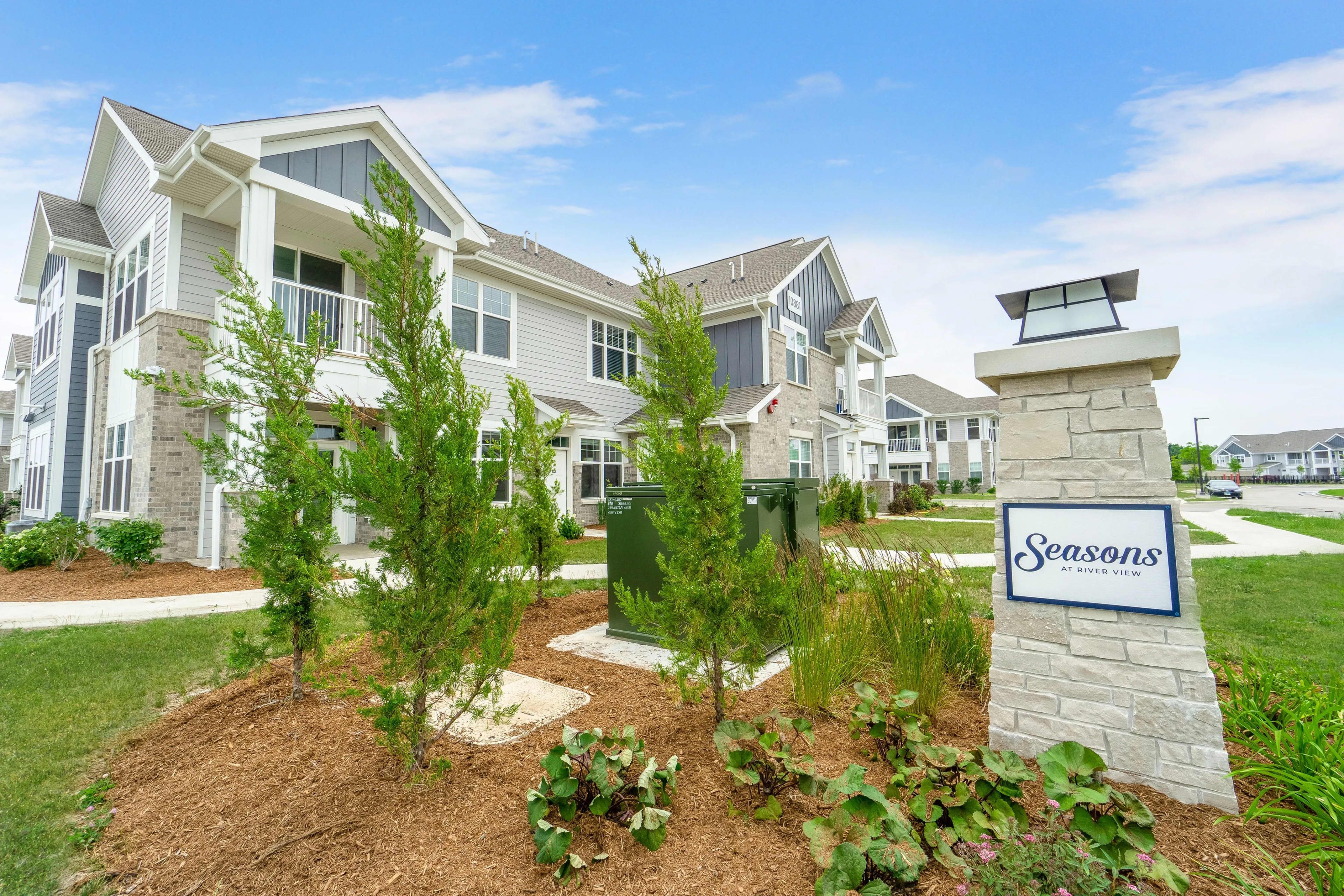 White and stone townhome exterior with front porch, young landscaping, and Seasons at River View property sign.