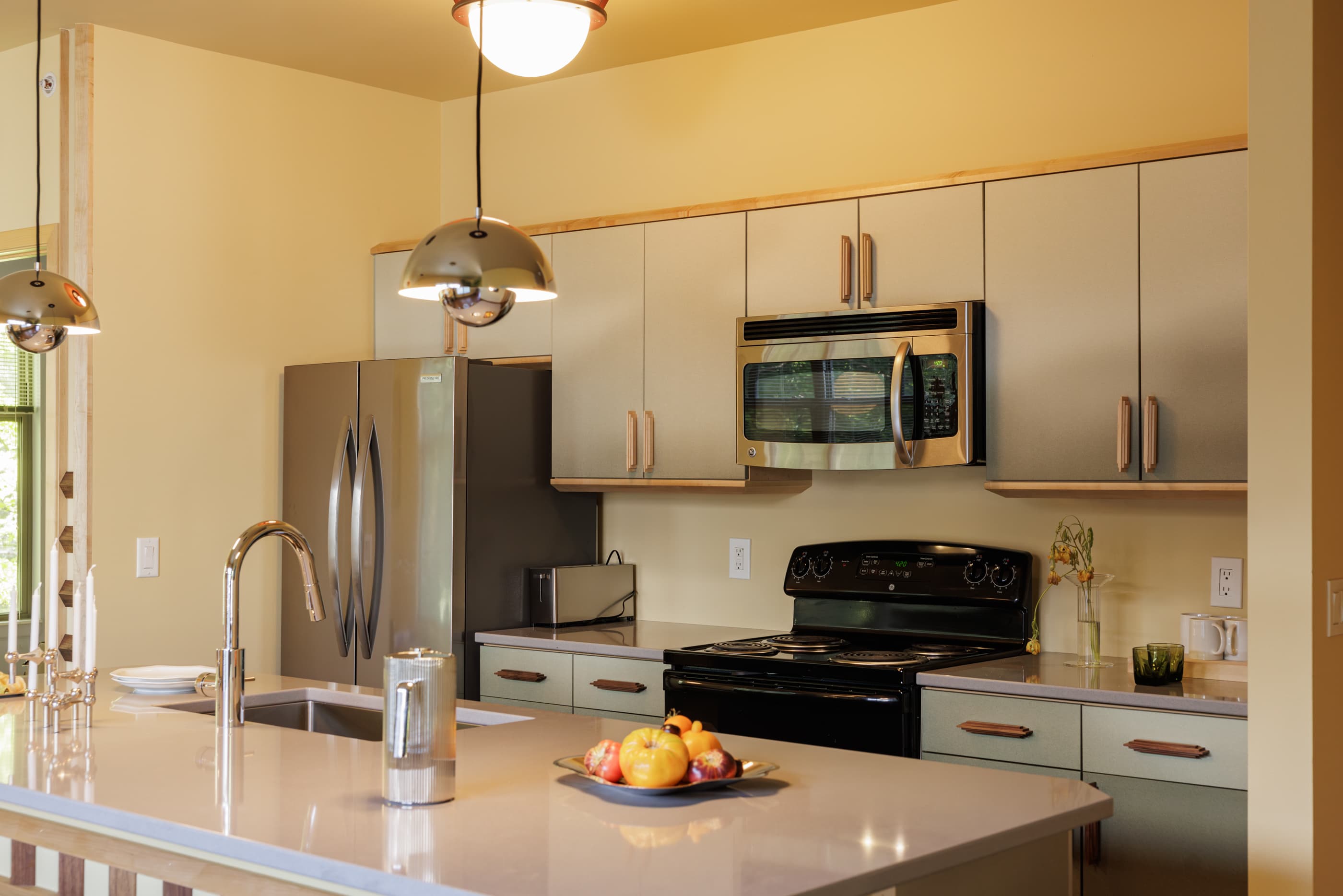 Kitchen with cream cabinets, stainless steel refrigerator and black range, pendant lighting, and quartz island countertop.