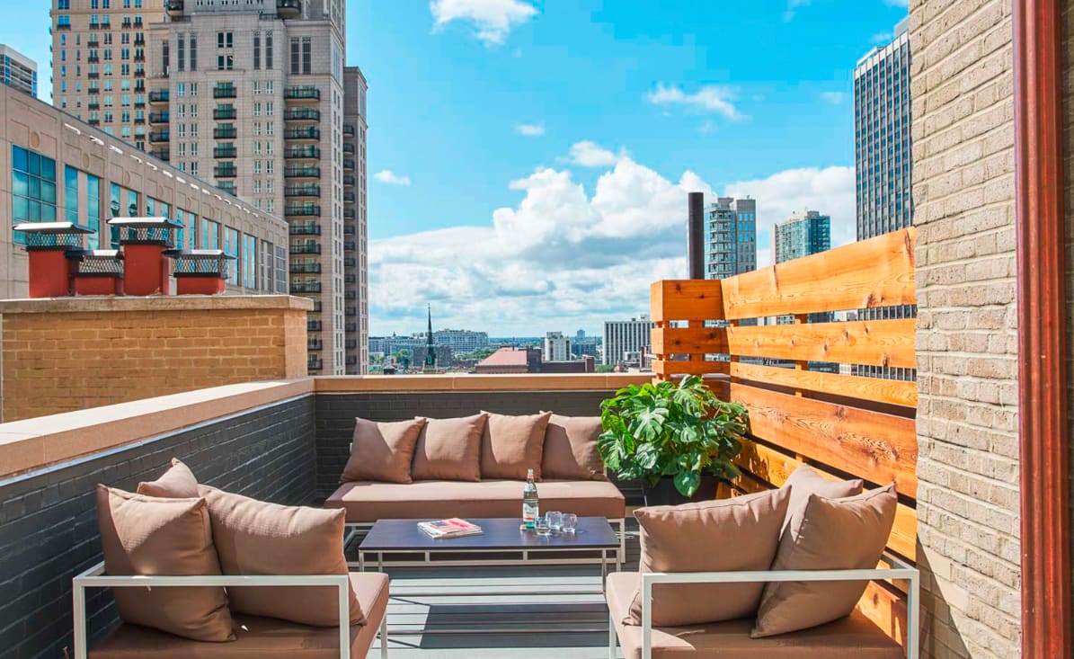 Rooftop terrace with brown cushioned seating, coffee table, potted plant, wooden privacy screen, and Chicago skyline views.