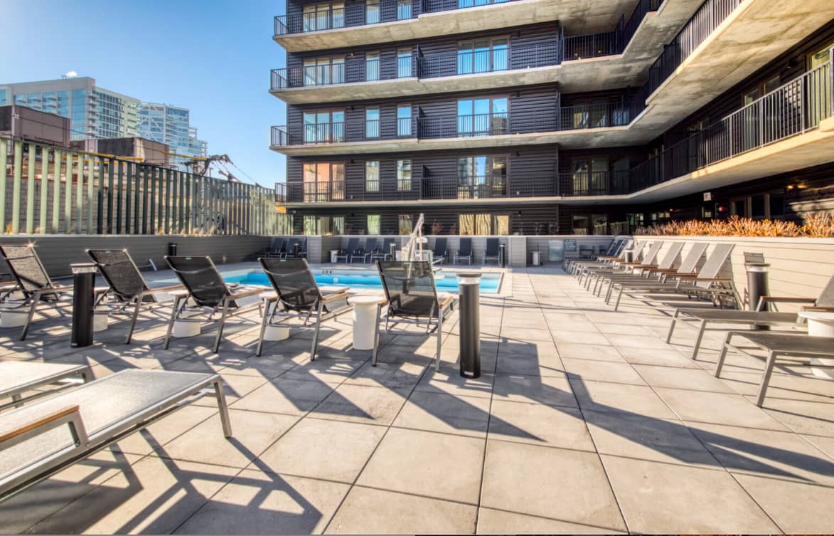 Rooftop pool deck with black lounge chairs, blue swimming pool, modern dark building facade, and Chicago skyline in background.