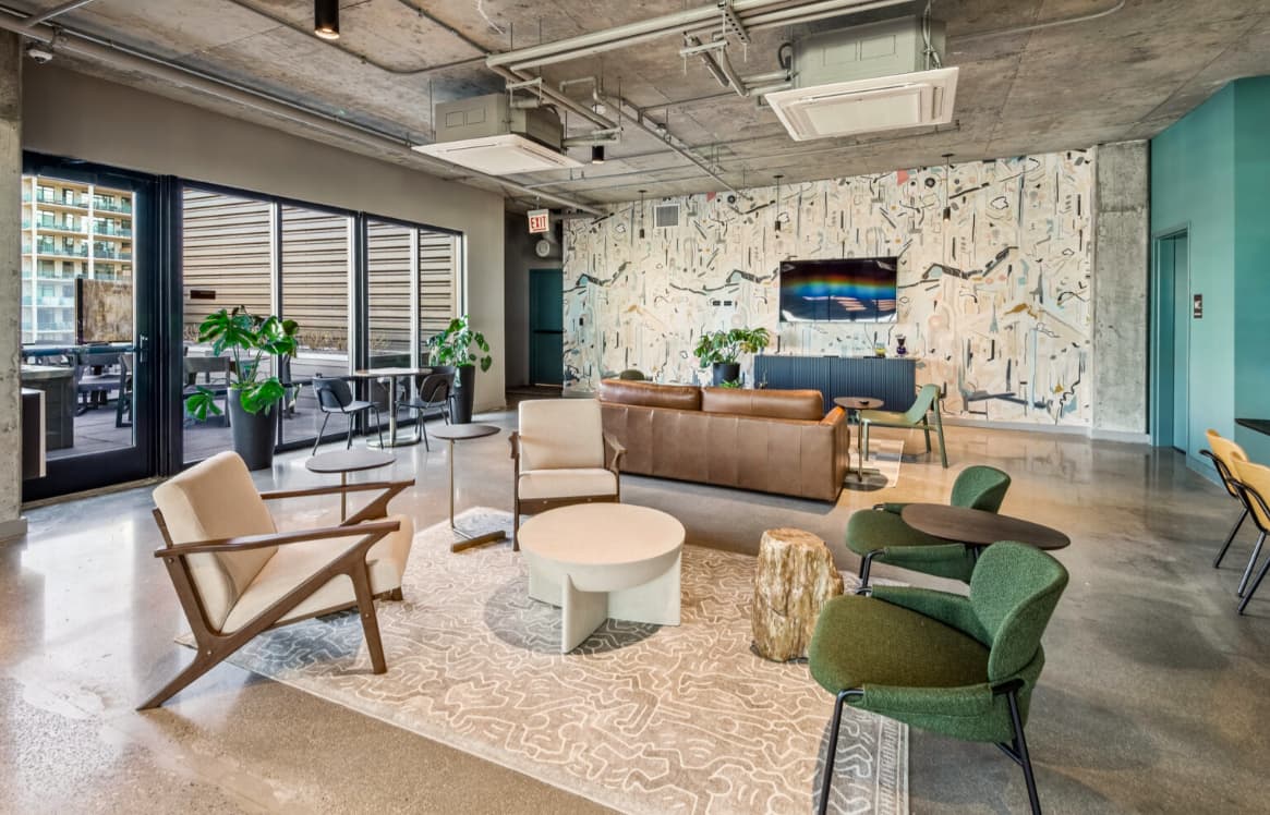 Open-concept lounge with tan mid-century chairs, brown leather sofa, green accent chairs, patterned wall art, and glass doors opening to a terrace.